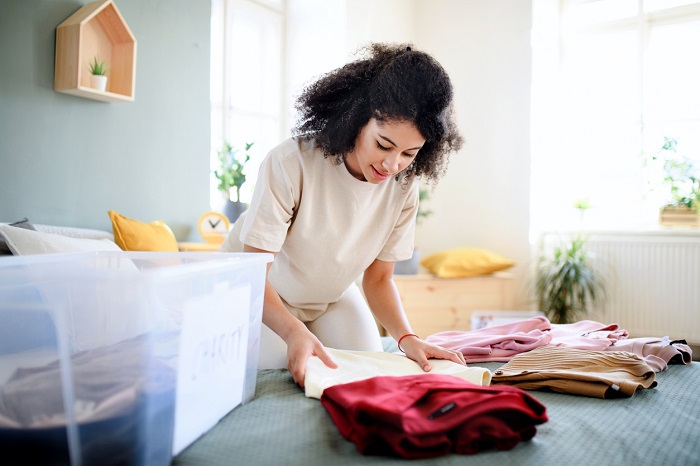 Young woman sorting and organizing wardrobe in her bedroom. 