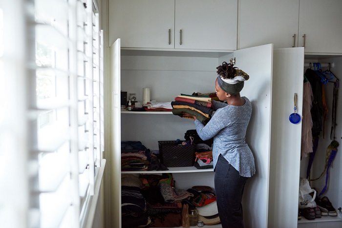 A young woman packing away clean laundry at home into a closet. 