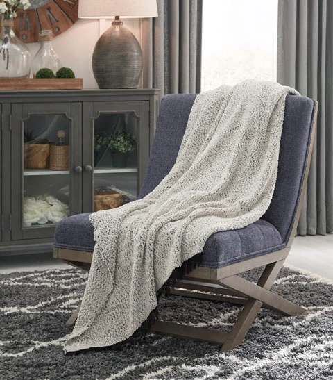 The Signature Design by Ashley Leonita collection throw blanket draped over a blue chair 