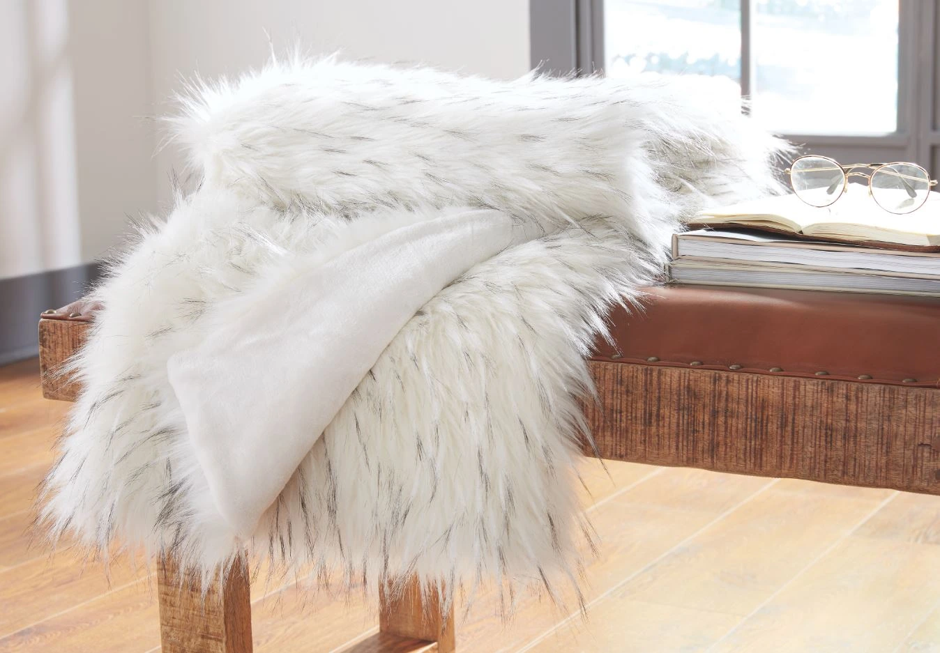 The Signature Design by Ashley Casila collection faux fur throw blanket on a bench 