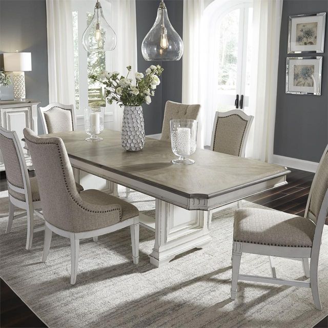 Luxurious dining room with two hanging lighting fixtures, a long, double layered dining table, and six gray upholstered chairs sitting around.  
