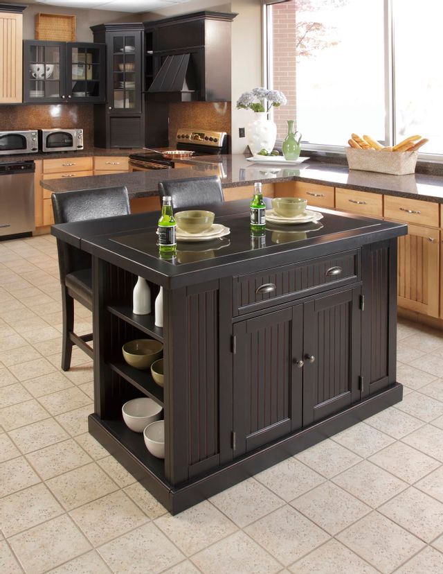 Dark wooden kitchen island with storage drawers and two leather backed chairs sitting in the middle of a modern kitchen. 