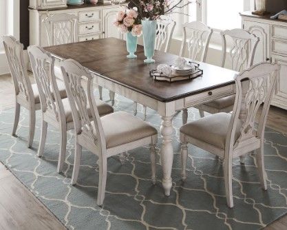 Modern dining room with a long wooden and white combo table with eight white wooden chairs all on top of a large area rug.
