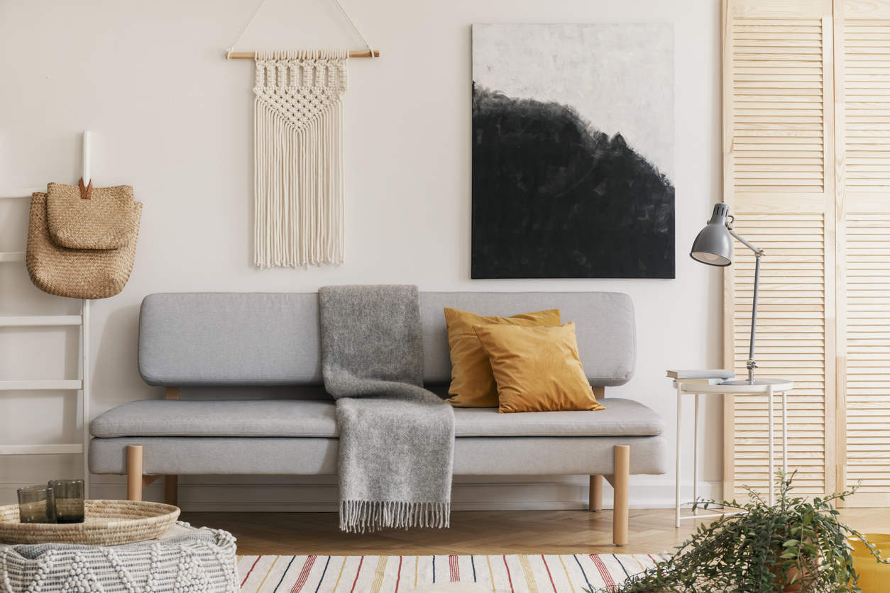 a modern grey couch with tan throw pillows and a grey blanket