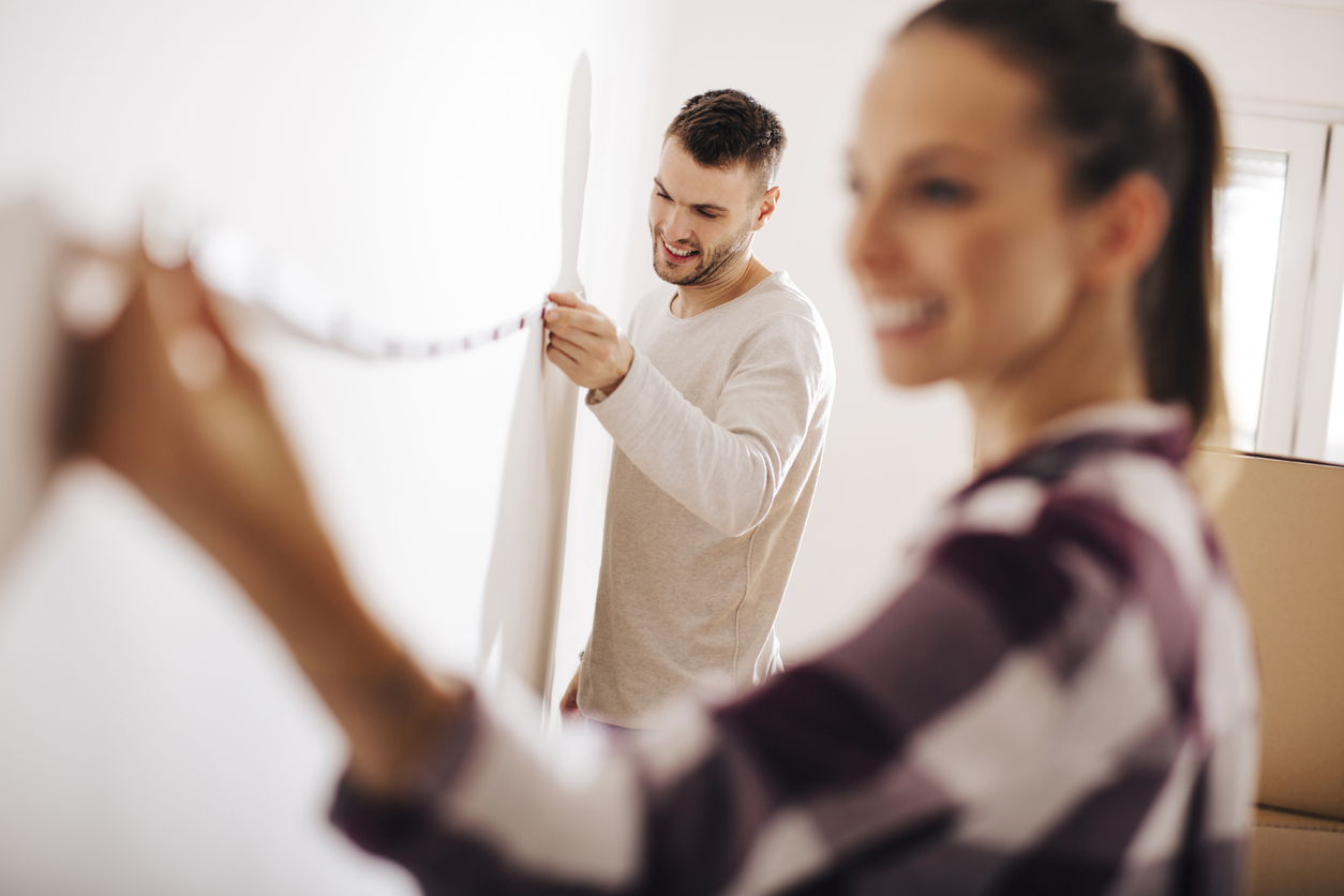 A couple measures a wall with a measuring tape