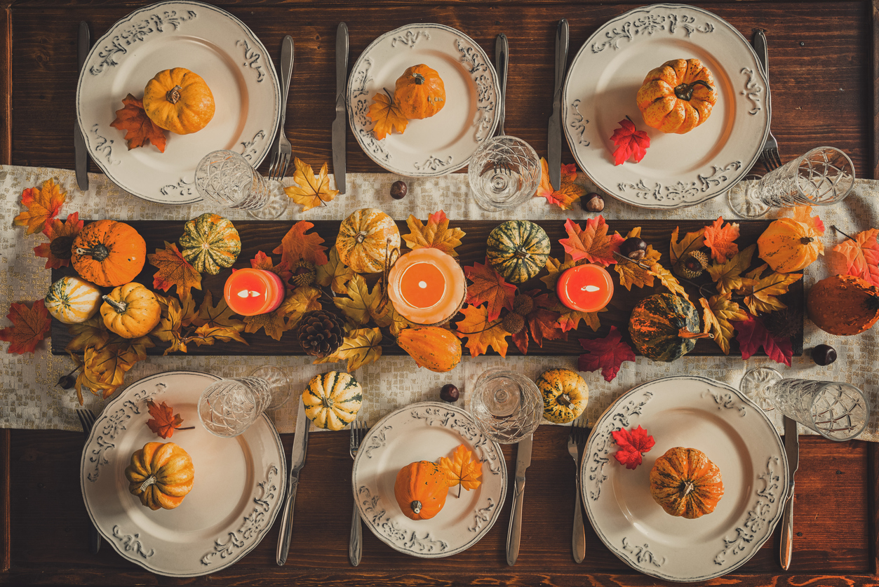 table setting for Thanksgiving dinner with candles, pumpkins, and autumnal leaves