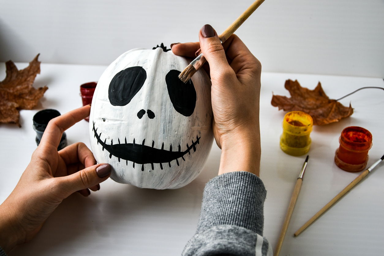woman paints face on orange pumpkin for Halloween