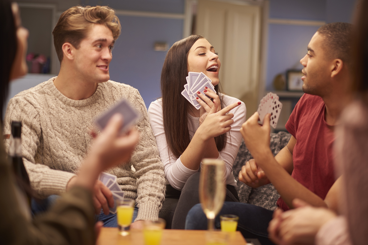 young friends sit on the sofa and play a game of cards at party
