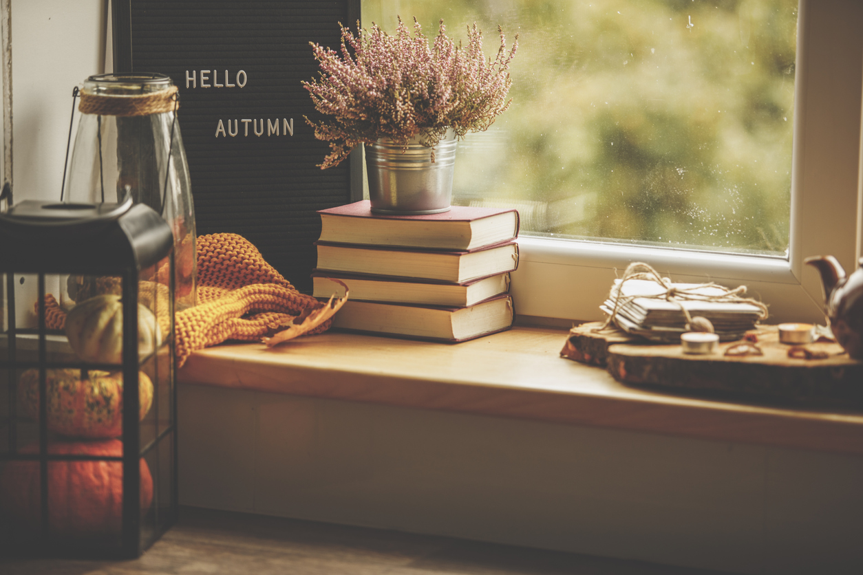 Hello Autumn sign placed against the window with books, flowers, orange scarf, lantern, and pumpkins