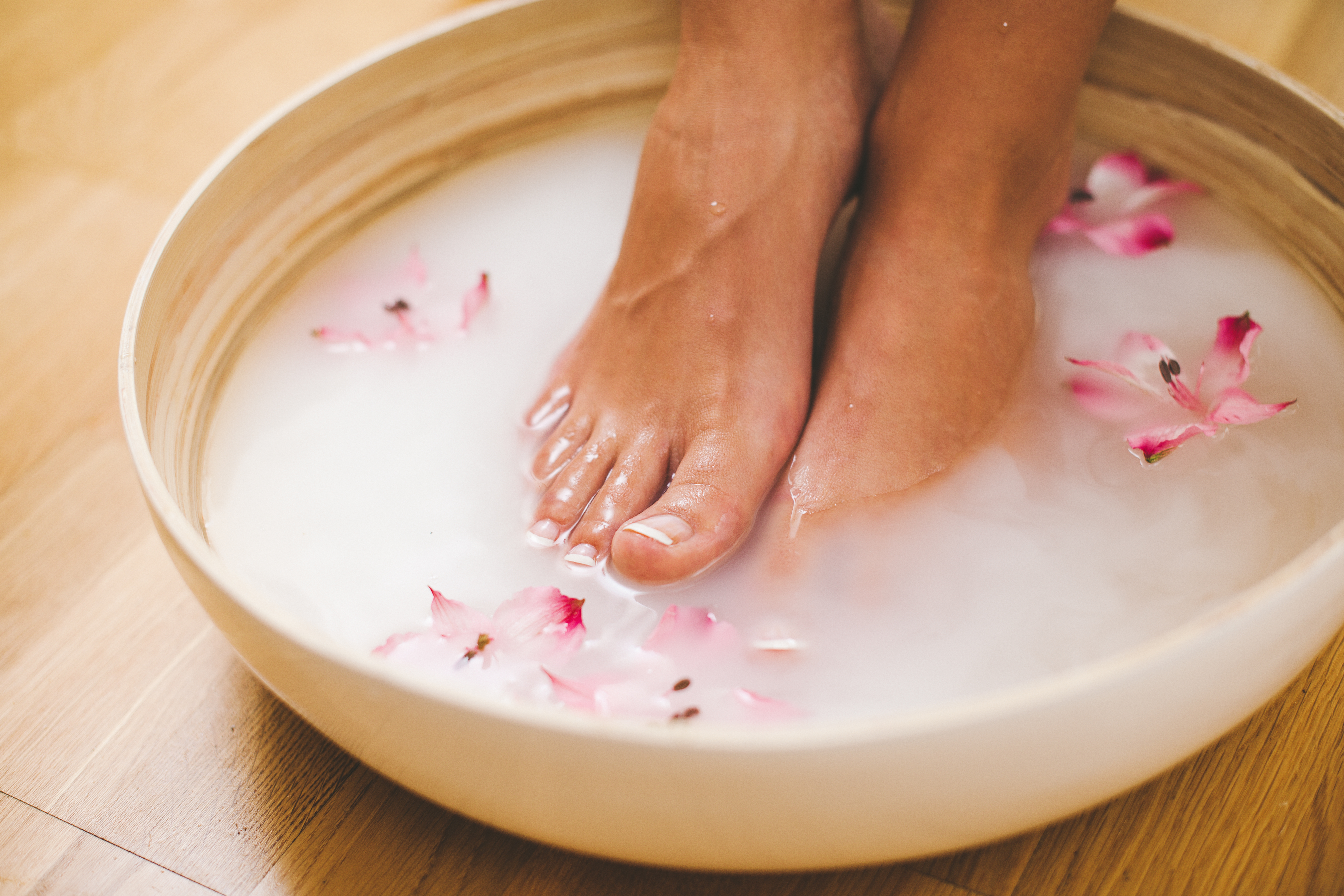 Woman dipping her feet in a foot bath with pink water and flowers 