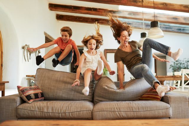 Front view of a mother and two young kids jumping on the couch