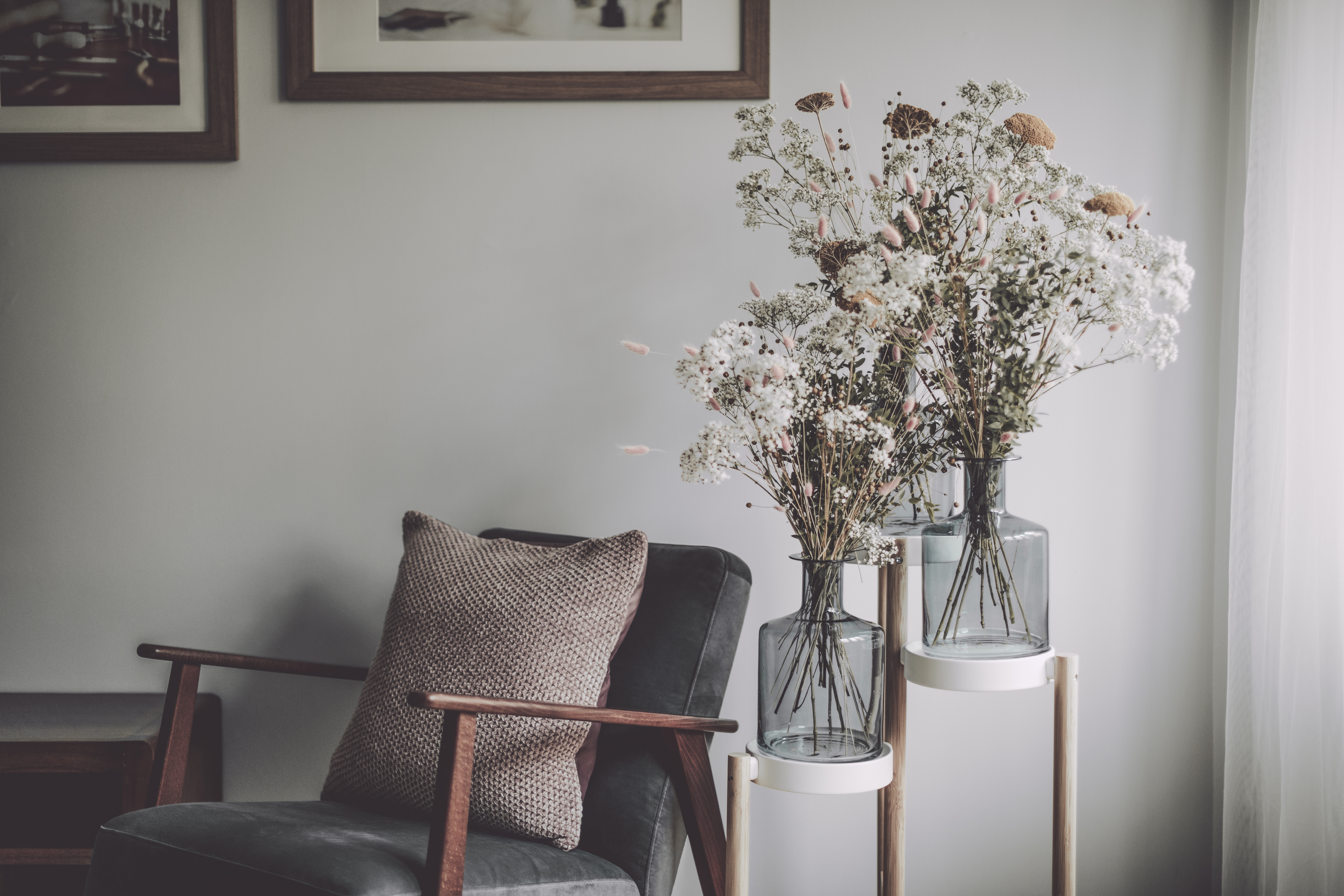 Mid-century modern-style accent chair in with pillow beside to flower vases filled with a mix of Baby’s Breath