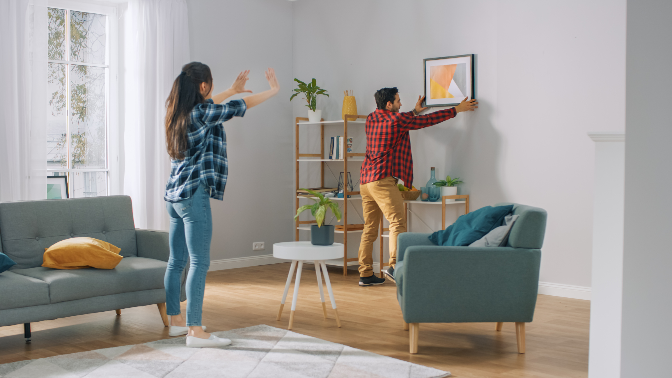  young couple arranging furniture and hanging art on the wall