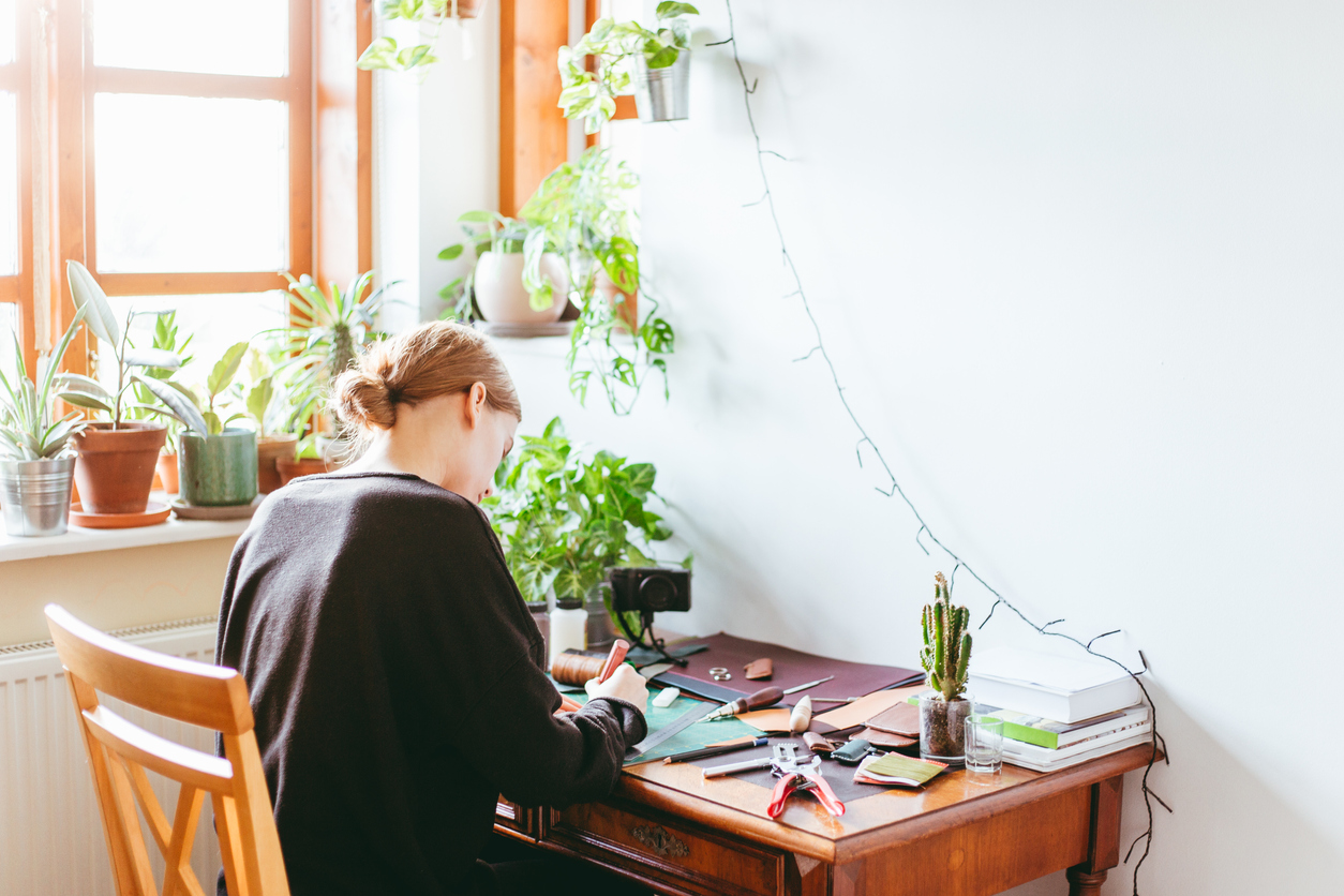 Woman at her crafting station in her guest bedroom by a sunny window with plants