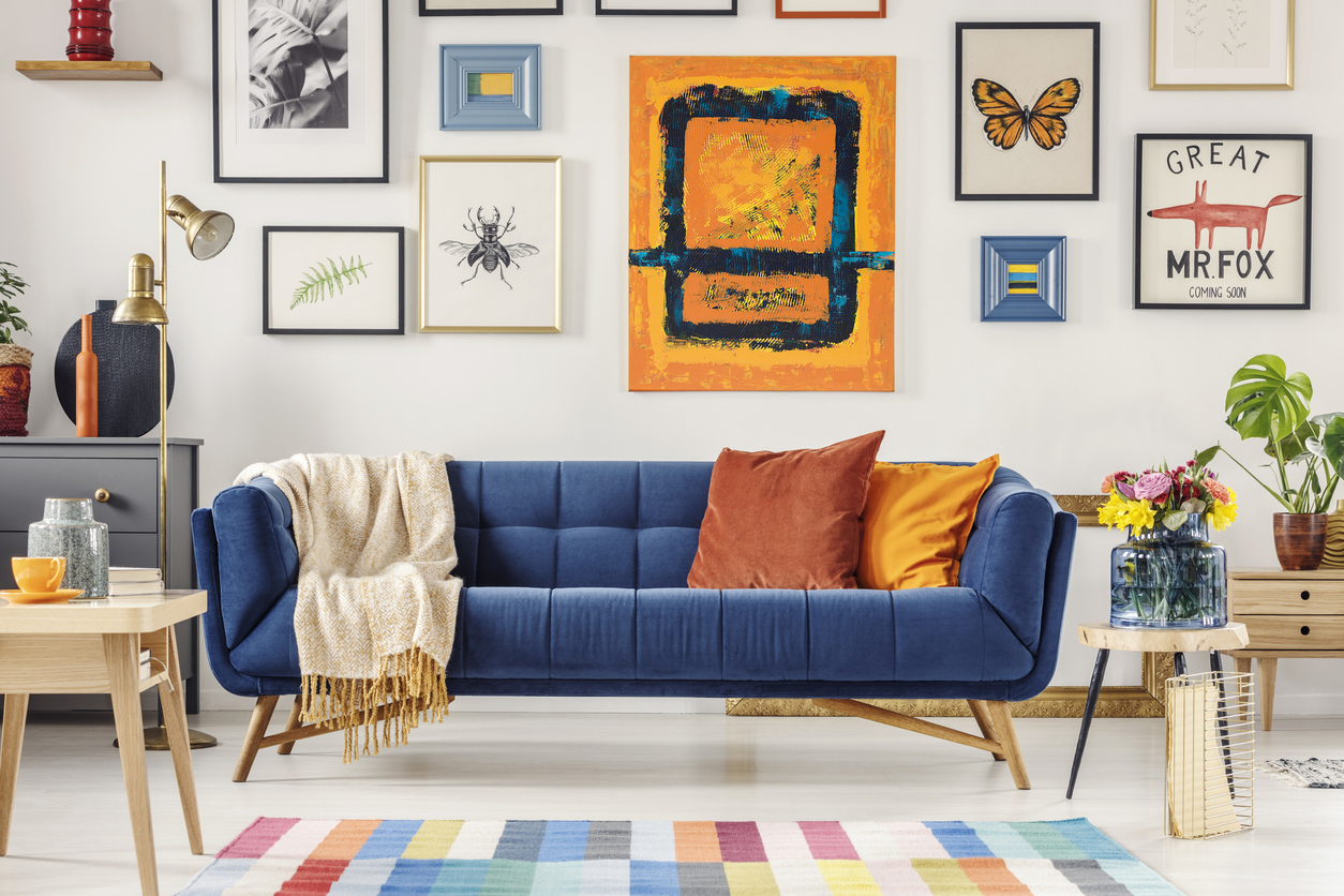 blue couch with bright blanket and two cushions standing in white living room interior with a gallery wall