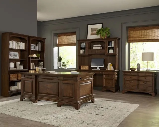 A wooden executive desk in a home office surrounding by matching wooden office furniture