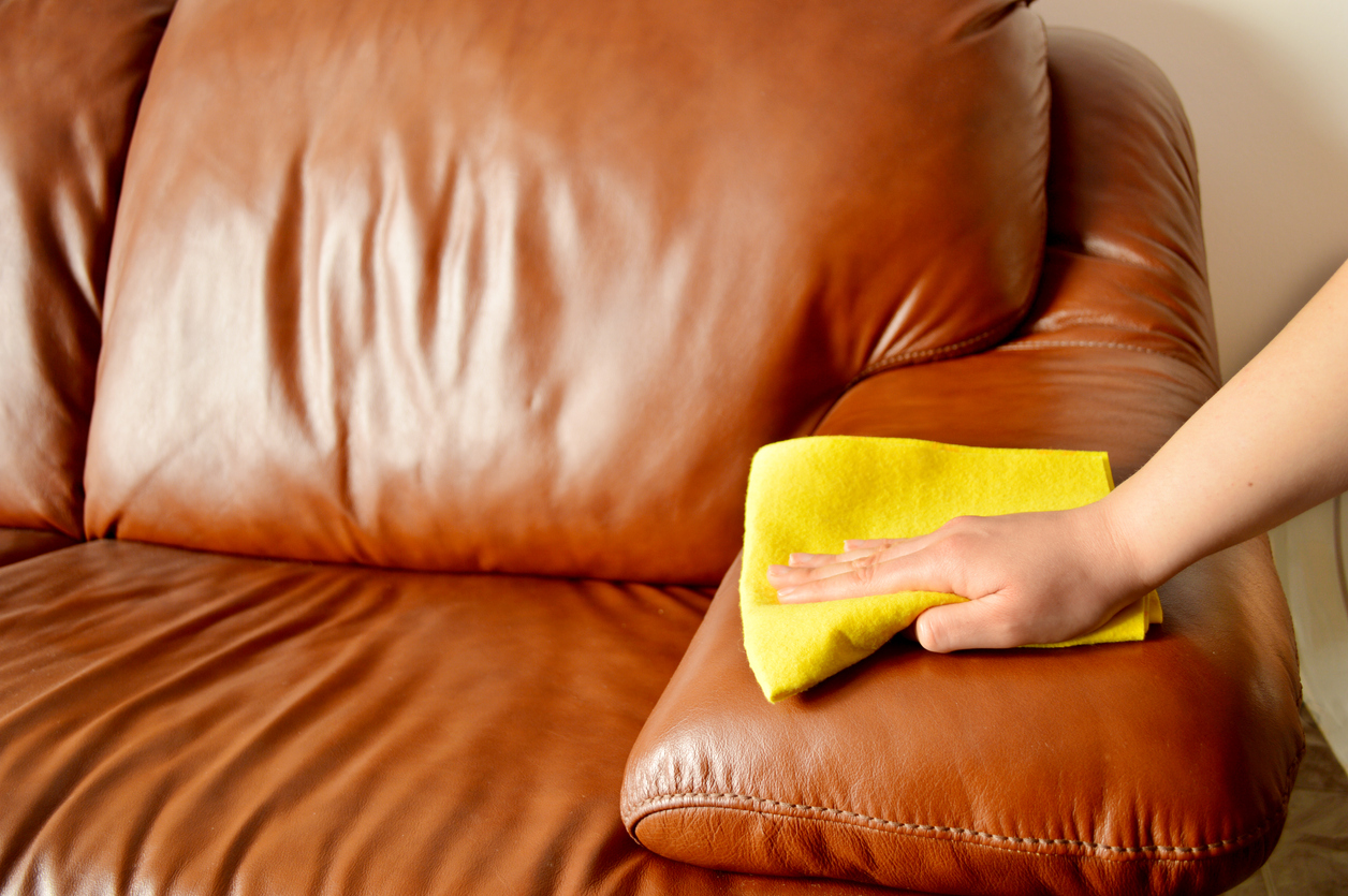 Hand with cloth cleaning a leather couch.