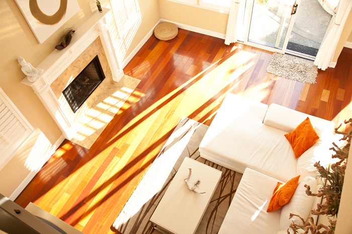 High angle view of an empty modern living room with a fireplace, hardwood floors, a white sofa and orange pillows.