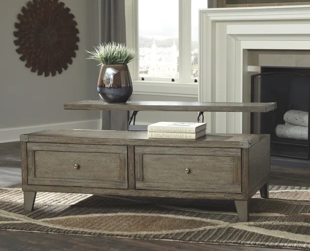 Photo of a wooden lift top coffee table in a modern living room with books and a plant sitting on top. 