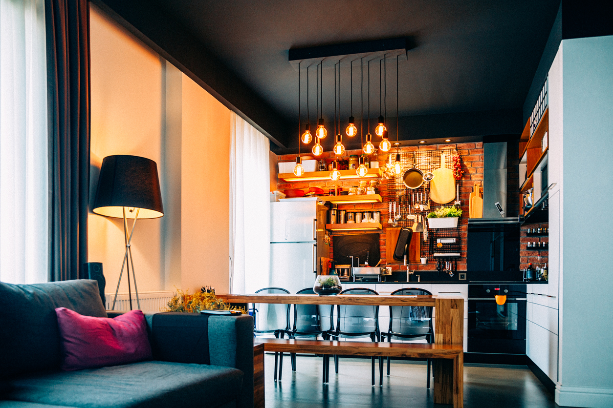 Industrial-style kitchen with wooden table, hanging metal lights, and sofa 