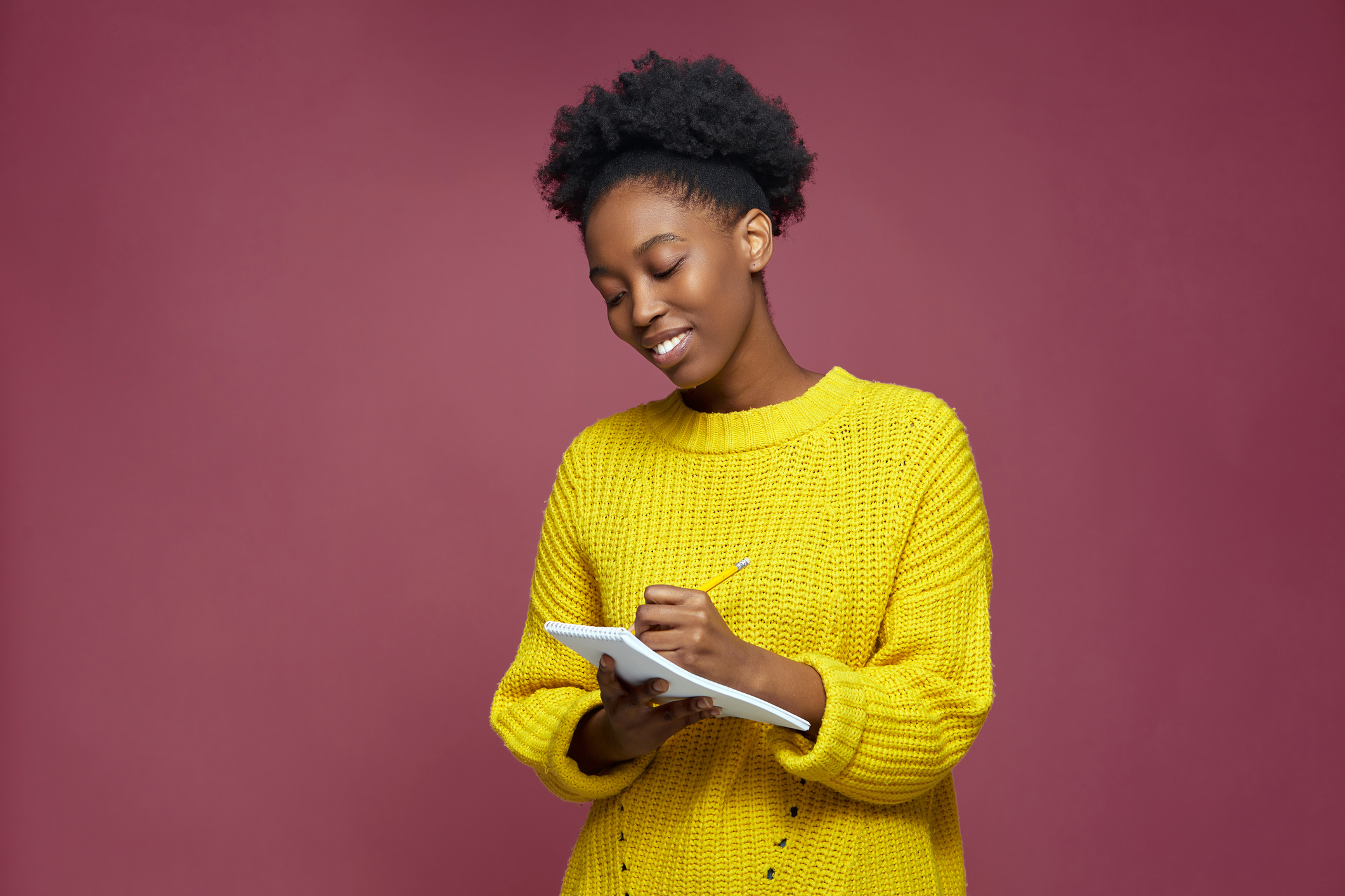 A woman in a yellow knit sweatshirt taking notes on a notepad 