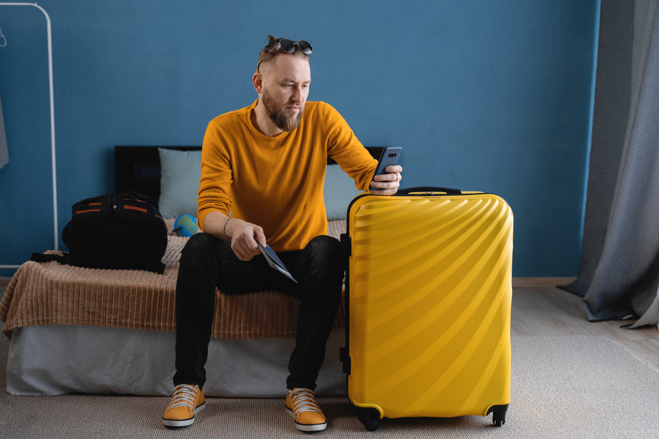 A man in a yellow sweatshirt with a yellow suitcase in a bedroom 
