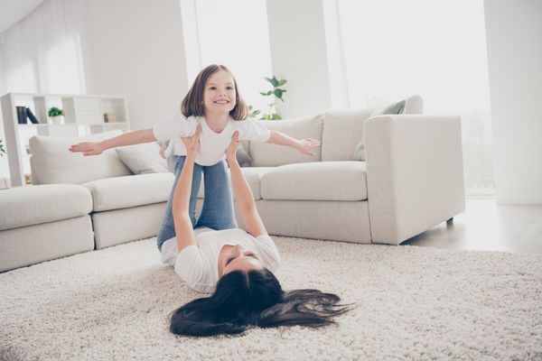 A woman sustaining a young girl on her legs on carpet 