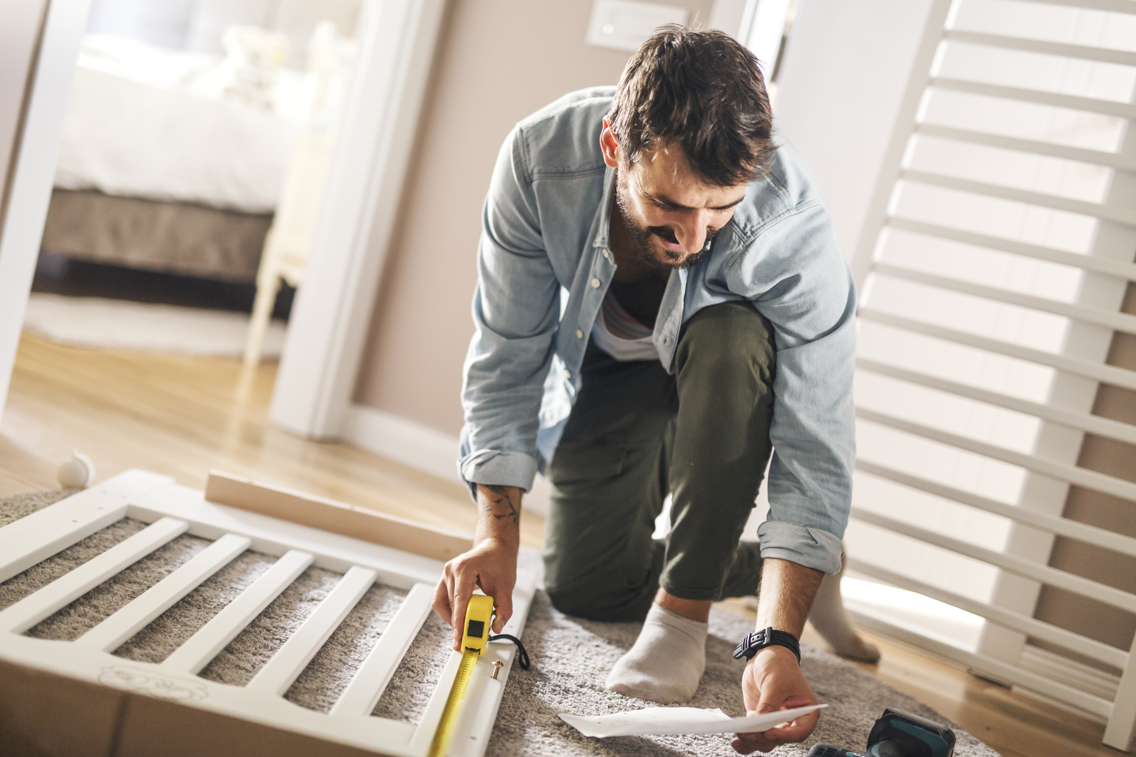 A man with a measuring tape reading building instructions for a bed 
