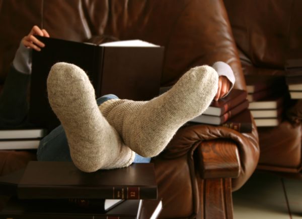 A person leaning back into a leather chair while reading books 