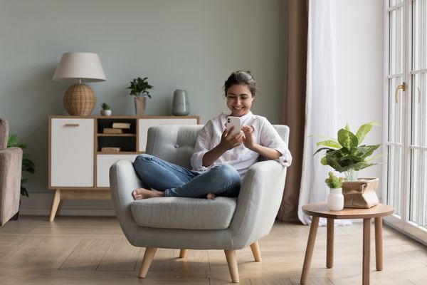 A woman smiling while using a smart device on a chair