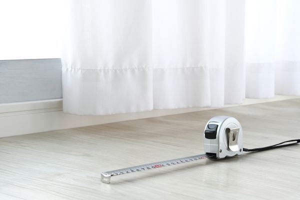 A tape measurer on the floor aside white curtains 