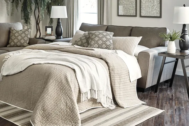 The Benchcraft Calicho collection queen sleeper sofa with its mattress opened together with bedding and décor. 