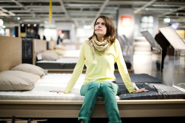 A woman in a yellow sweatshirt sitting on a bed in a furniture store