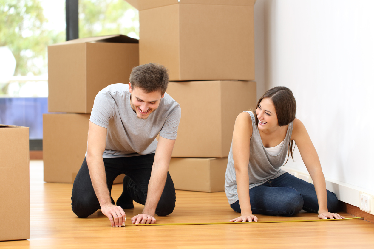smiling couple use tape measure in living room to place new furniture