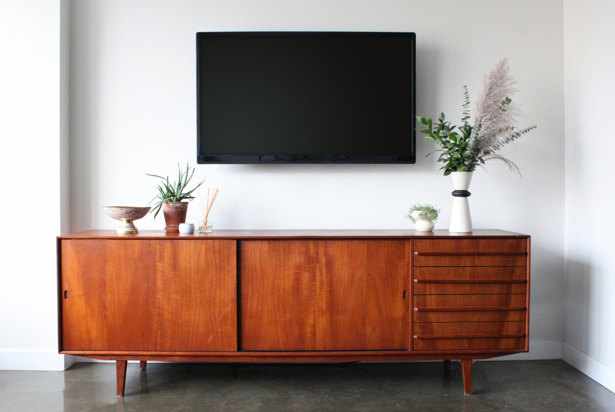 a mid-century modern media console situated underneath wall mounted TV