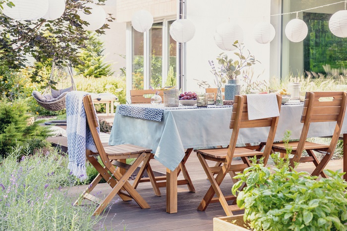 Wooden chairs at table with flowers and food in the garden with plants and lanterns.