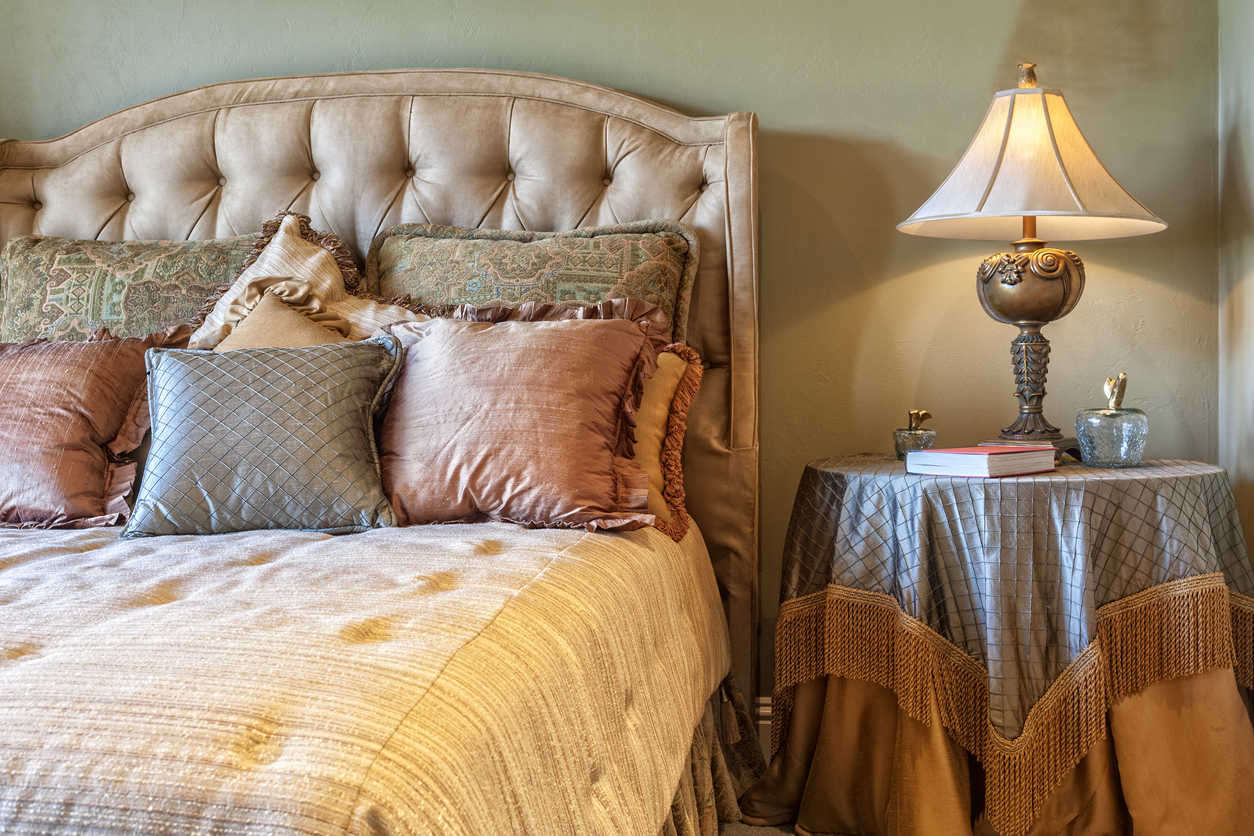 closeup of bed dressed with tufted comforter and satiny throw pillows