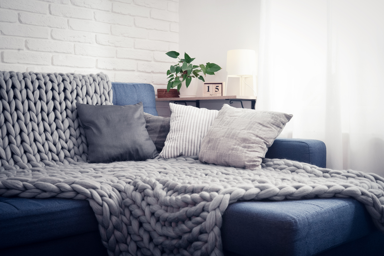 a sectional with four throw pillows and a knit blanket