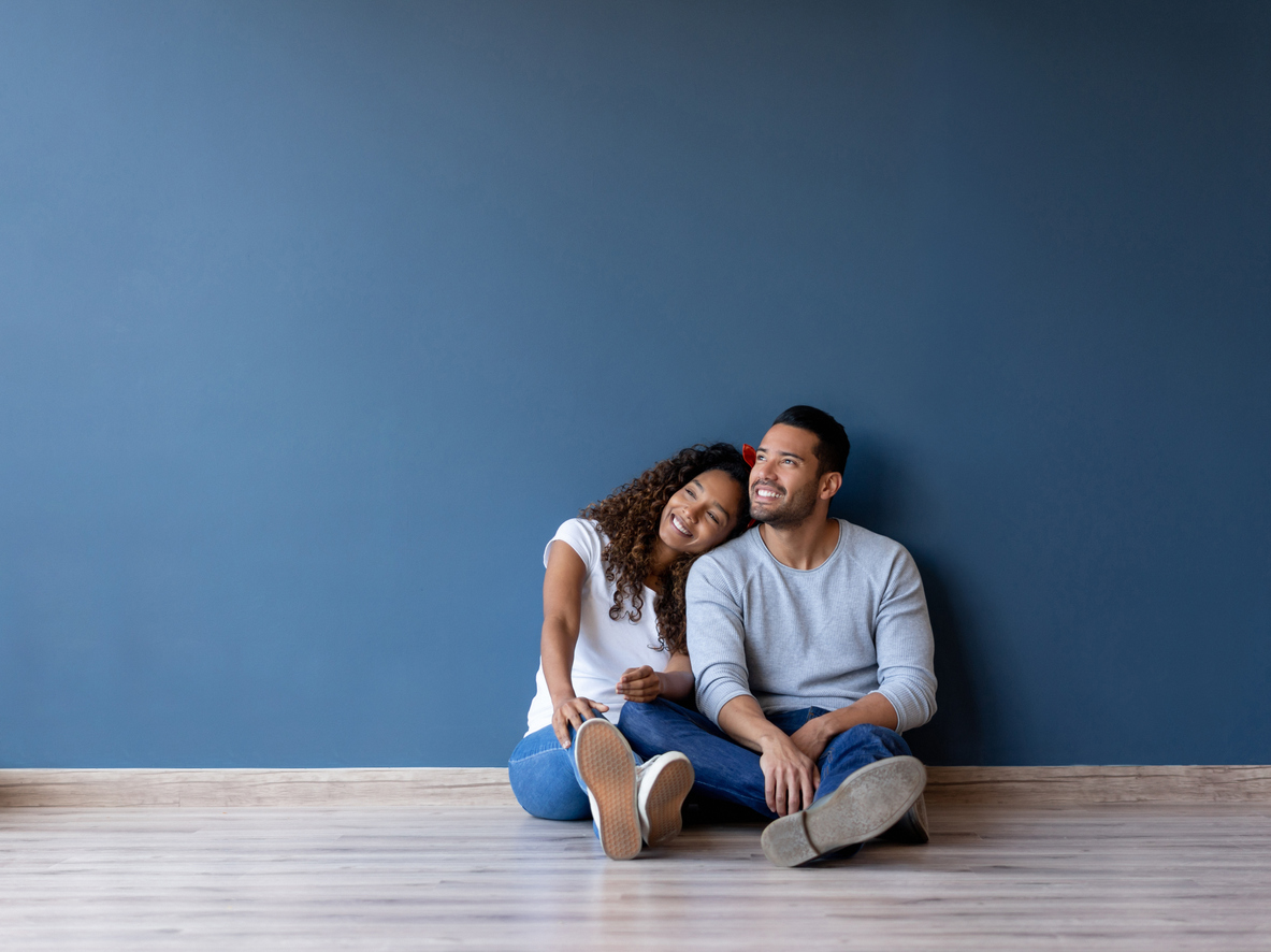 live-in couple smiles while sitting on the floor in unfurnished room