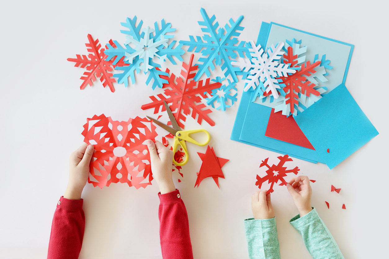 kids’ hands cutting snowflakes out of red and blue paper 