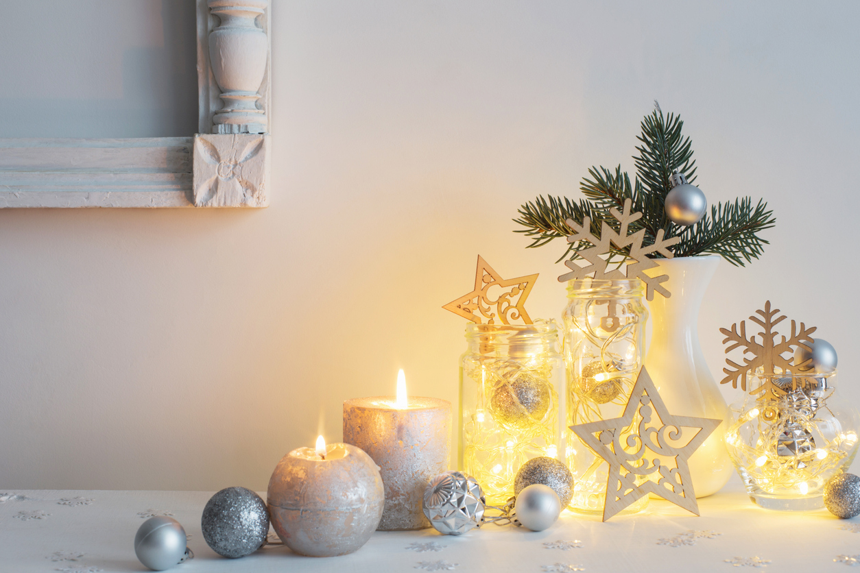lit silver and white candles with string lights inside mason jars and a sprig of Spruce tree 