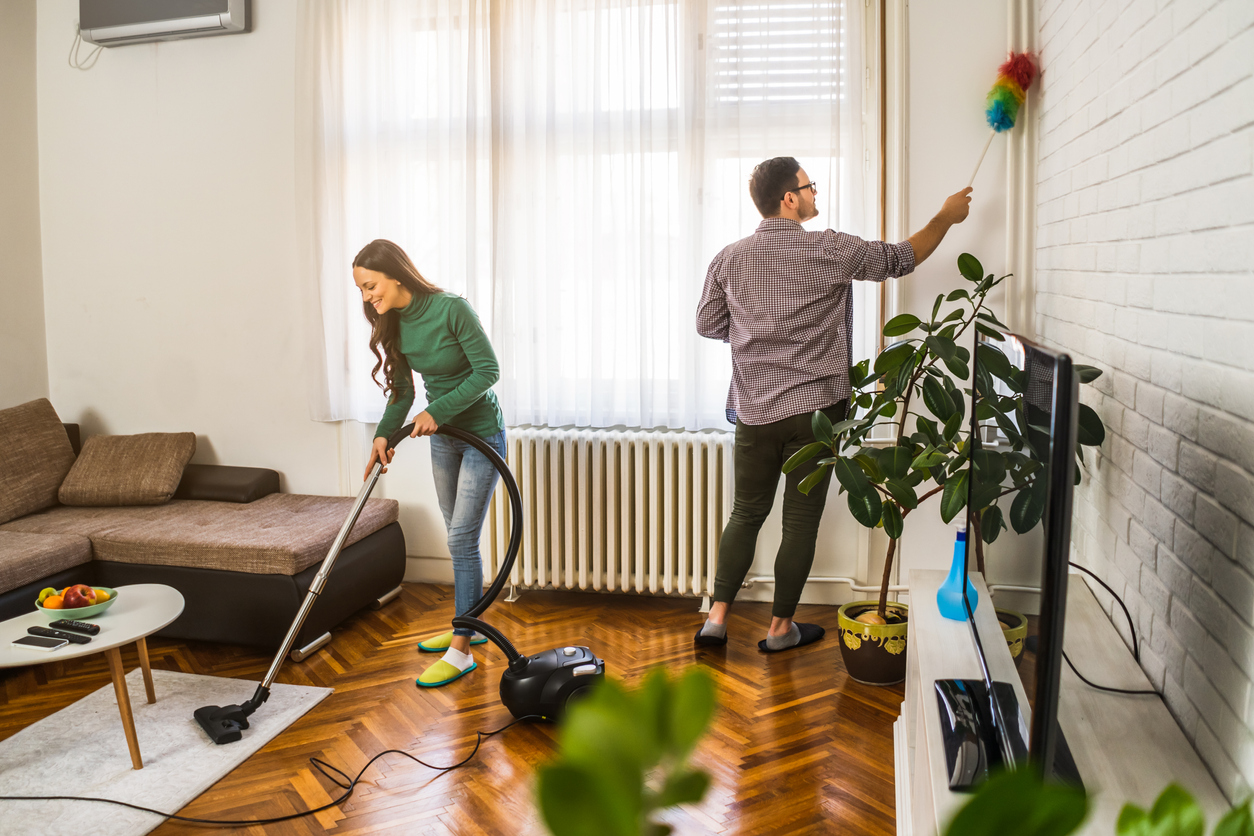 young woman and man vacuum and dust their loft style living room. 