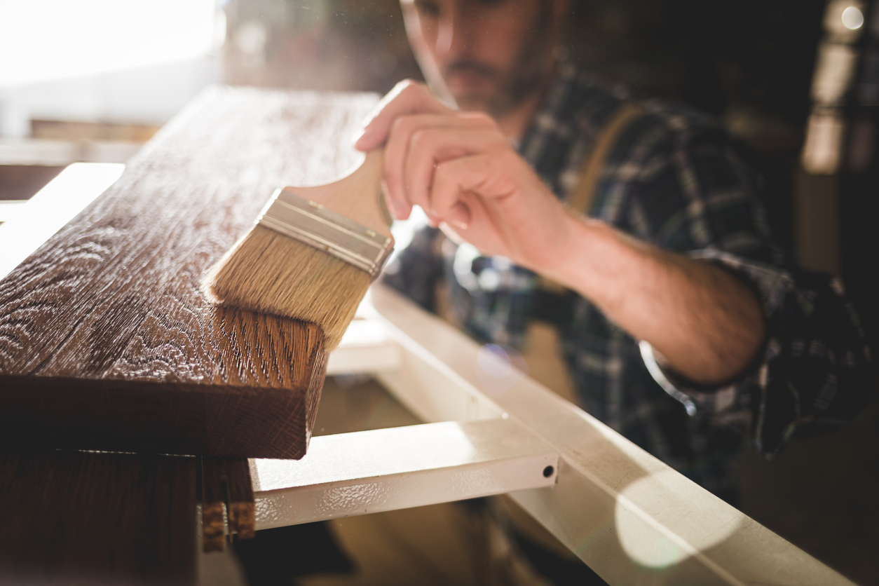 paintbrush applies paint or varnish on wooden board in carpentry workshop