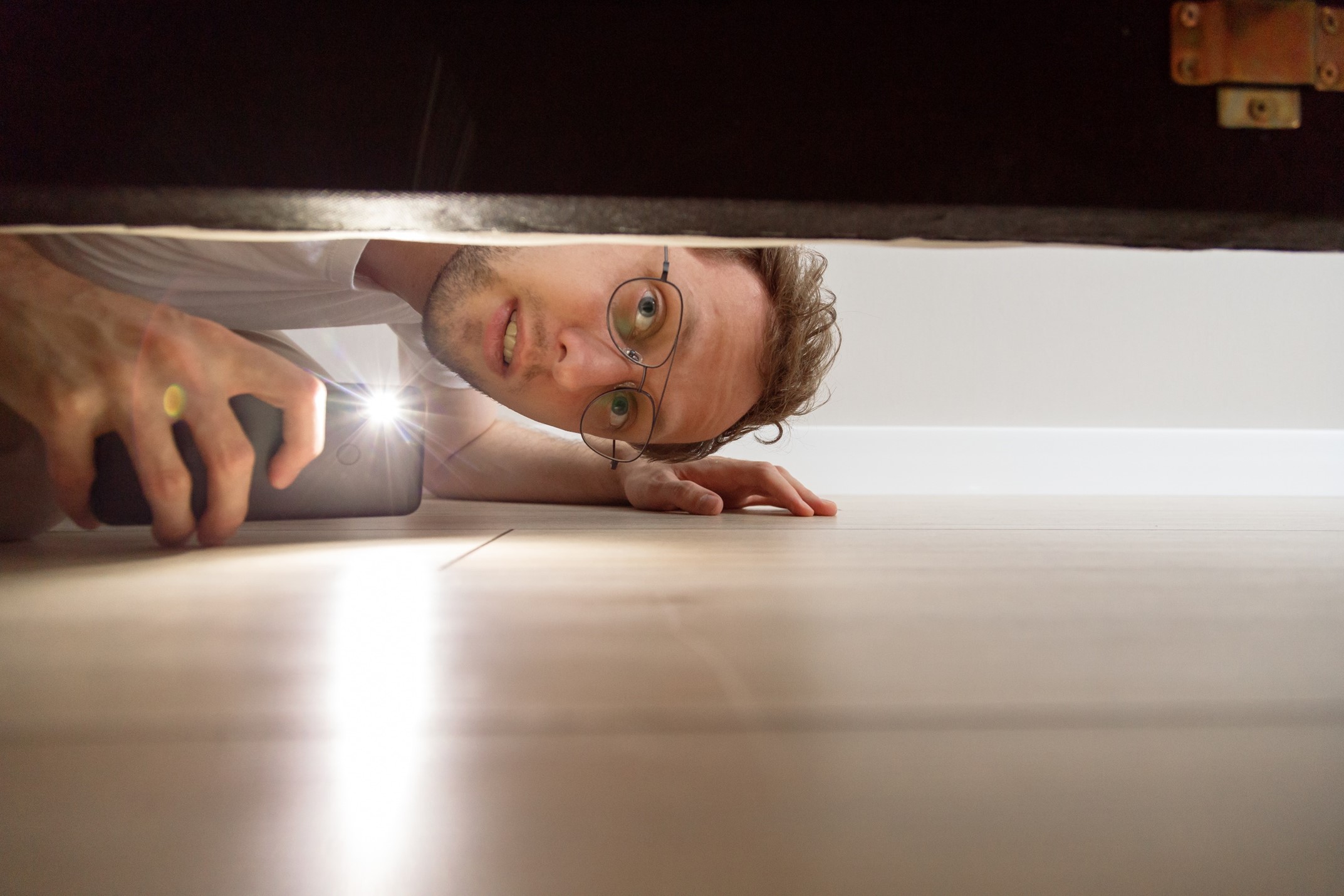 A man checking under his bed with a smart phone light 