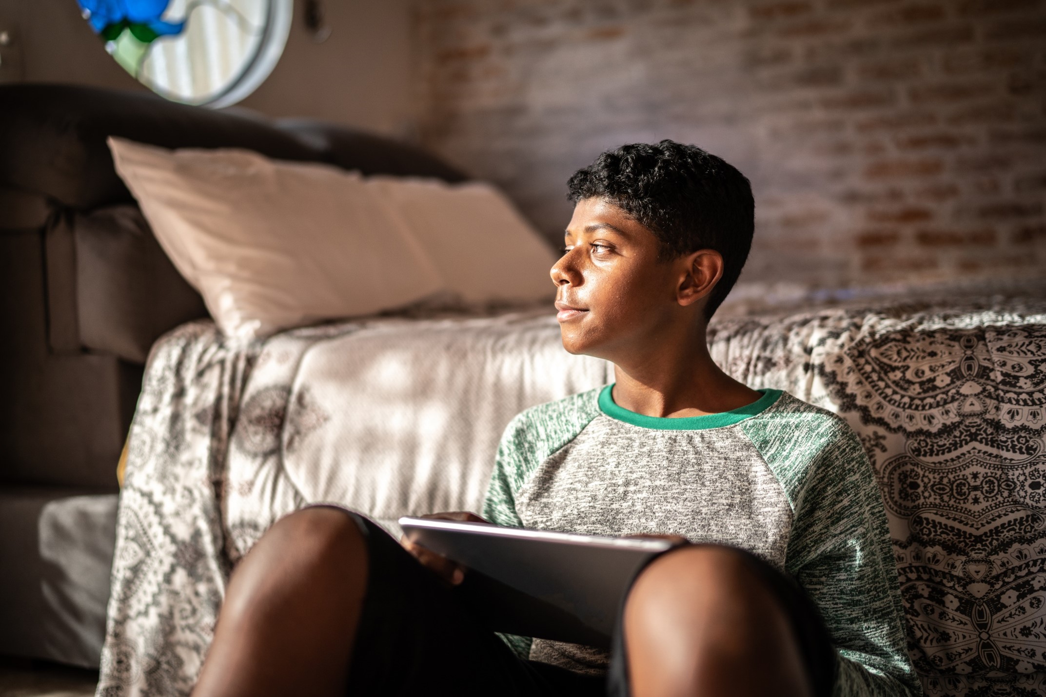 A teenage boy sitting next to a bed on the floor 