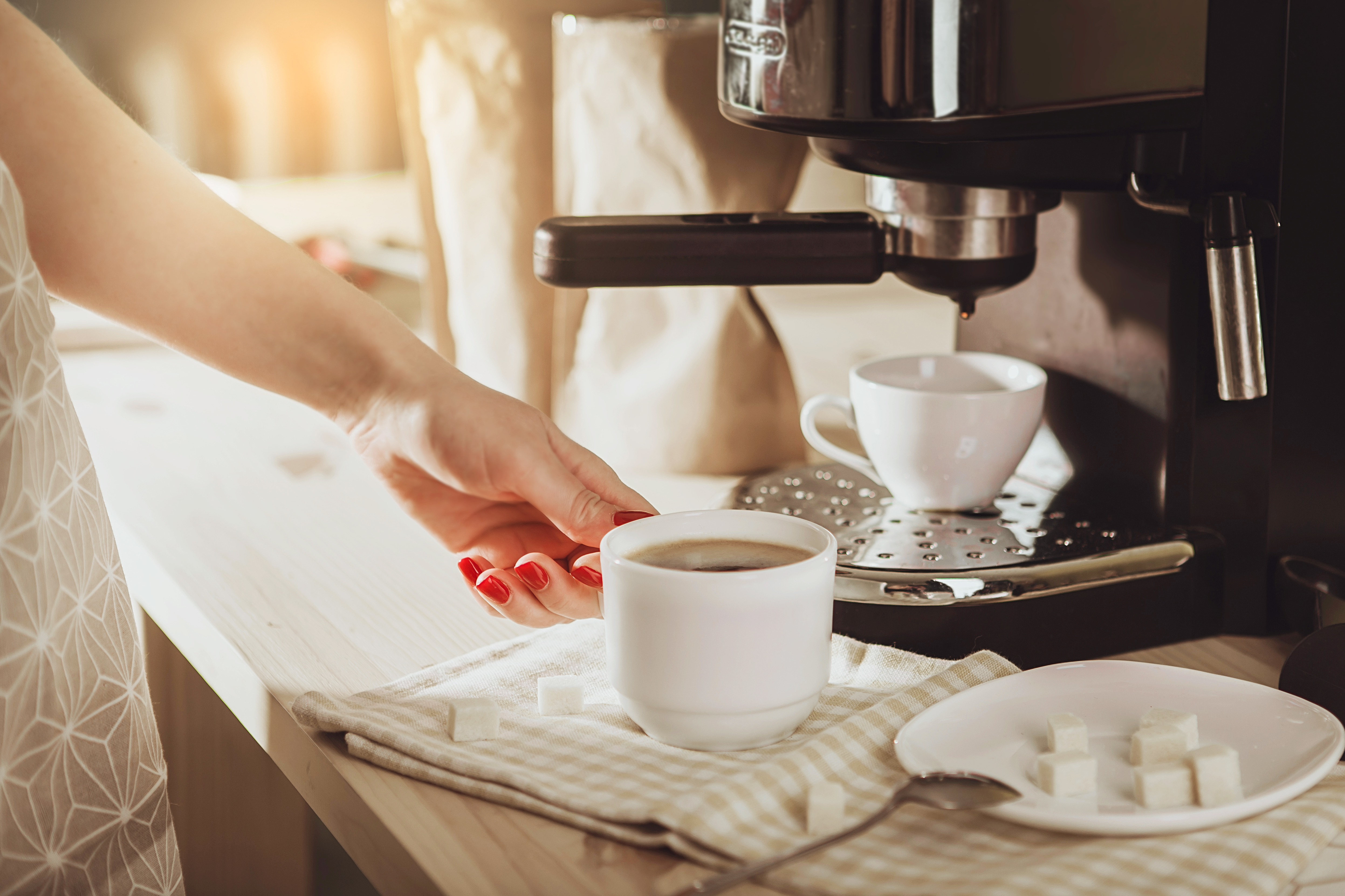 Woman with red nail polish making a cup of coffee at a home coffee station 