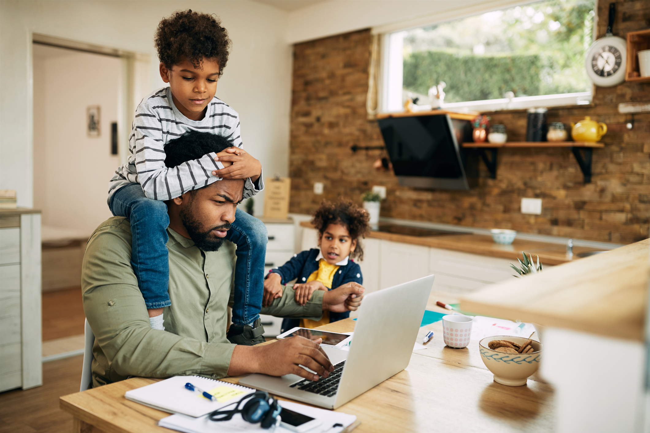 Dad works on laptop while children play around him