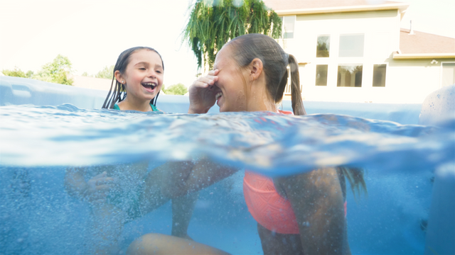 View of two girls smiling in a Nordic hot tub. The camera is half in the water and half out.