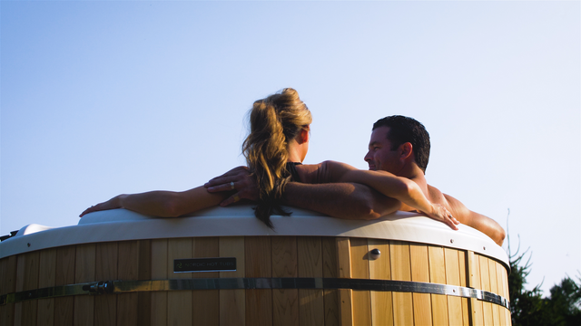 view from behind of a man and woman sitting with their arms around one another in a round Nordic hot tub