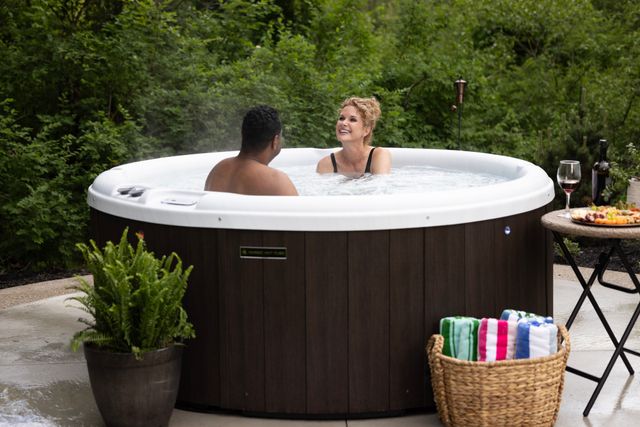Front view of a man and woman sitting in a round Nordic hot tub